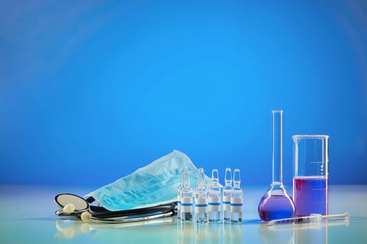 Beaker, medical flask with purple chemical reagent. Six ampoules with liquid, syringe, mask and phonendoscope, blue background. Pandemic Coronavirus photo