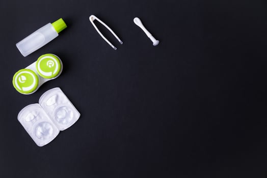 Contact lenses set with container, tweezers, suction cup and bottle with solution on black background, top view, copy space photo