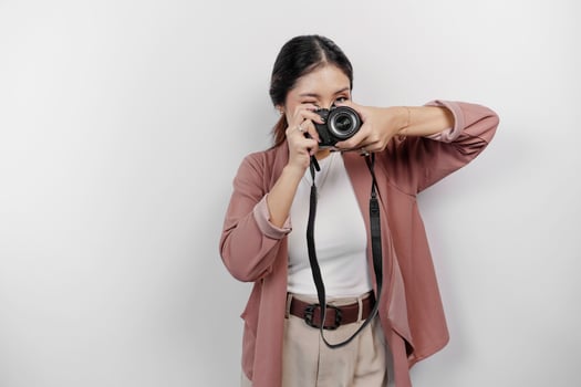 Happy smiling young Asian woman tourist standing with camera taking photo isolated on white studio background