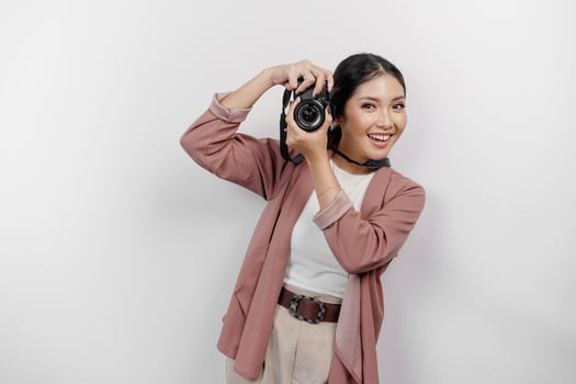 Cheerful young Asian woman tourist standing with camera taking photo isolated on white studio background