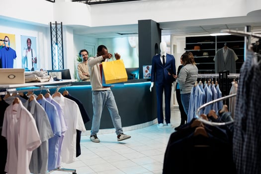 Shopping center boutique satisfied customer holding bags with apparel purchase. Happy cheerful african american man with packages having fun after buying clothes with discount photo