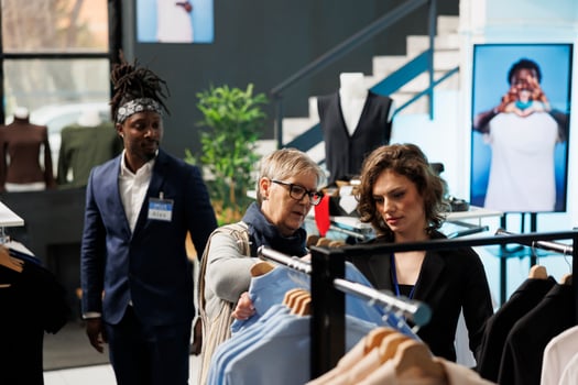 Small business worker helping senior customer choosing trendy clothes, discussing fabric in modern boutique. Elderly woman shopping for casual wear, buying fashionable merchandise in clothing store photo