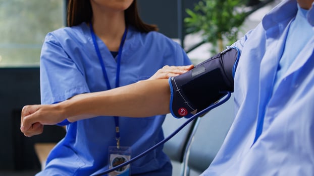 Assistant doing hypertension examination with tonometer in hospital waiting room, measuring asian patient blood and pulse pressure. Cardiologist nurse checking hypotension with cardiology instrument. photo