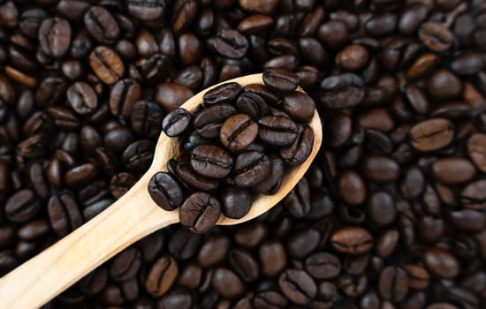 Aromatic coffee beans in a wooden spoon on a coffee background. Close-up. Top view. Selective focus. photo