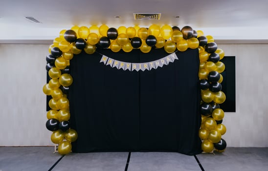 Birthday decoration indoors with yellow and black balloons, gray carpet, black cloth and white wall background. photo