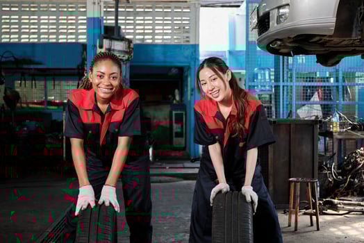 Two diverse female automotive mechanic worker partners compete to push car wheels for change and repair at garage, vehicle maintenance service jobs, industry occupation, and professional labor works. photo