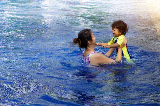 Asian child boy learn swimming in a swimming pool with mom. - Sunset filter effect photo