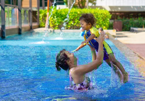 Asian child boy learn swimming in a swimming pool with mom. - Sunset filter effect photo