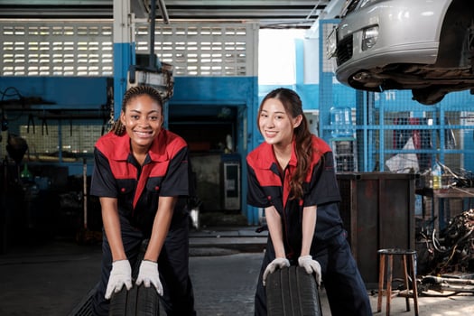 Two diverse female automotive mechanic worker partners compete to push car wheels for change and repair at garage, vehicle maintenance service jobs, industry occupation, and professional labor works. photo