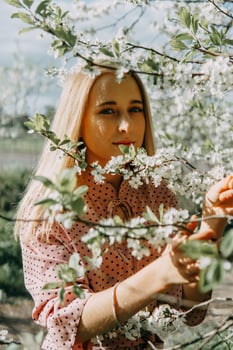 Blonde girl on a spring walk in the garden with cherry blossoms. Female portrait, close-up. A girl in a pink polka dot dress. photo