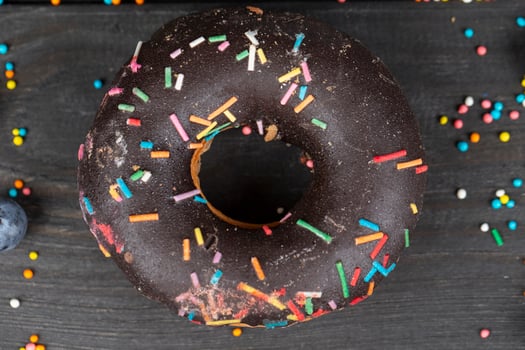 Beautiful sweet food. Colorful chocolate donut with colored sprinkles on a wooden background. photo