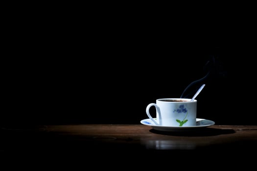 a cup of hot coffee brewed with a spoon on a wooden table on a black background photo