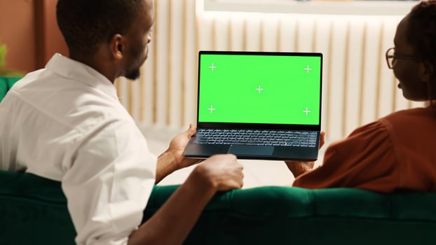 Bored tourists watching video on laptop chroma key green screen mock up waiting for check in process to be over. Guests sitting in hotel foyer while porter employee carries luggage to their room photo