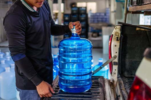Workers lift drinking water clear and clean in blue plastic gallon into the back of a transport truck purified drinking water inside the production line to prepare for sale.small business photo
