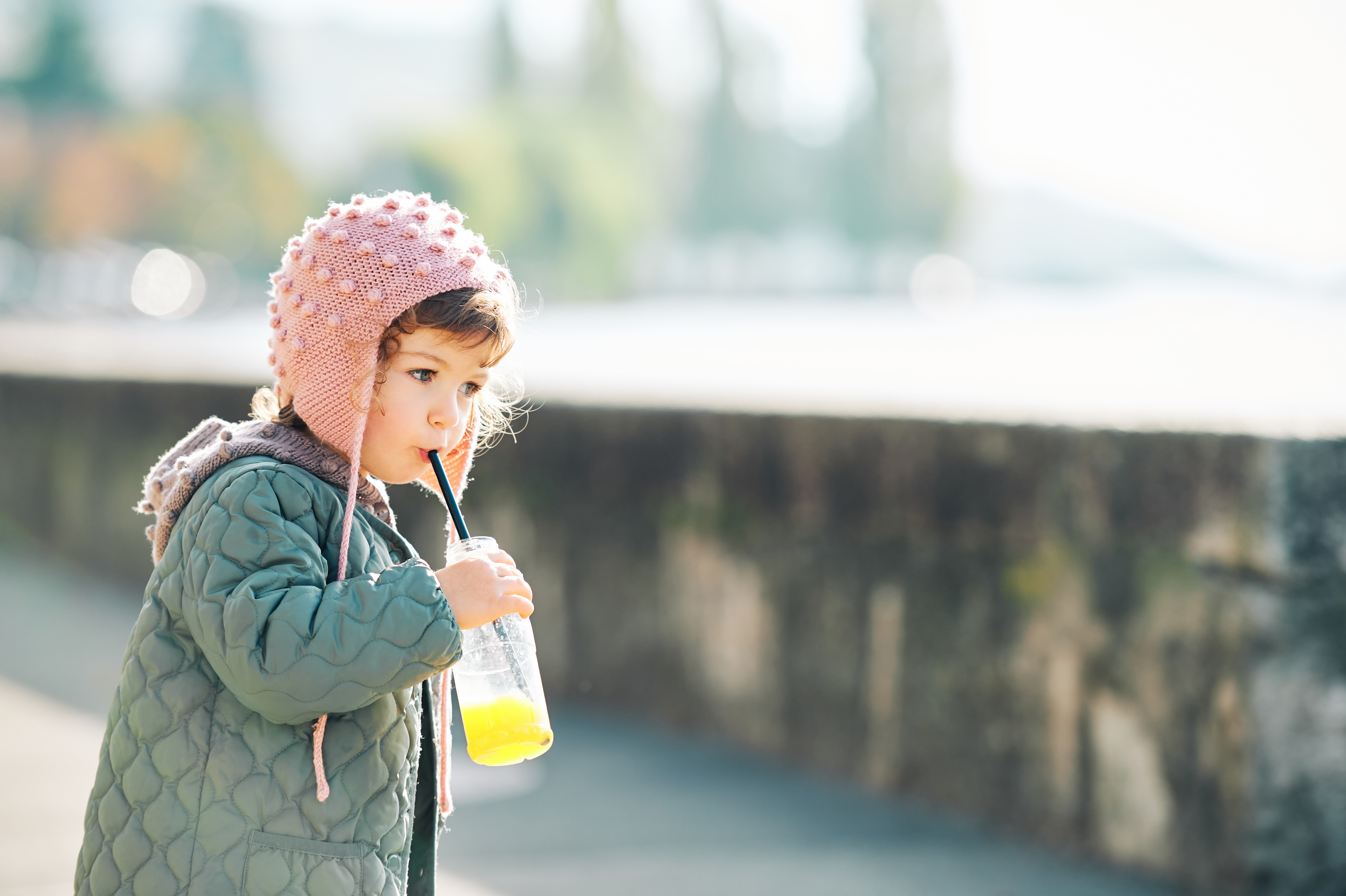 Outdoor portrait of cute little girl drinking orange juice on her morning walk photo