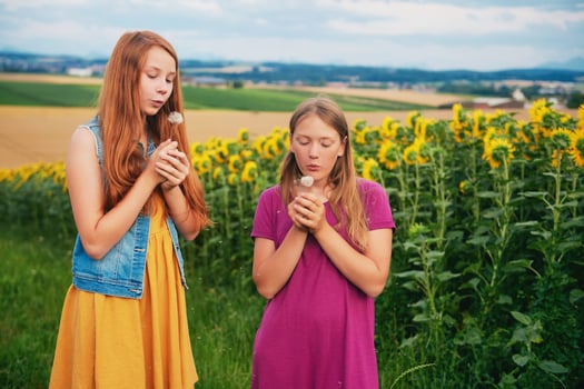 Outdoor portrait of two happy young girls playing with dandelions in countryside photo