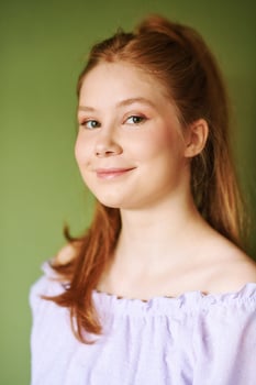Beauty portrait of pretty young 15 - 16 year old redhaired teeenage girl wearing purple dress posing on green background photo