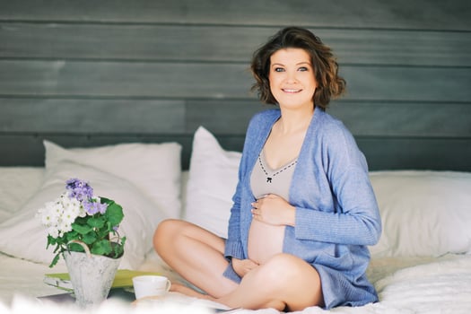 Early morning portrait of happy young pregnant woman resting in bed, drinking tea photo