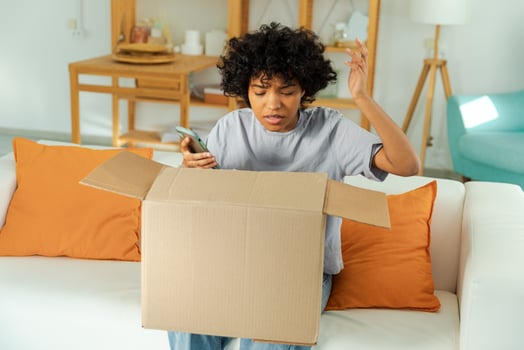 Unhappy angry african woman unpack delivered box receiving damaged shipping mistake problem in postal service. Annoyed confused customer client receiving wrong parcel checking online app on smartphone photo