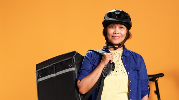 Close up portrait shot of upbeat smiling BIPOC bicycle rider holding professional thermic bag, isolated over studio background. Happy courier delivering meal order to client photo