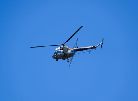 A helicopter of agricultural aviation is flying in the blue sky. photo
