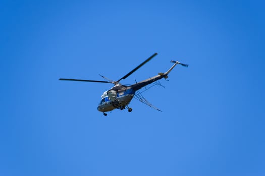 A helicopter of agricultural aviation is flying in the blue sky. photo