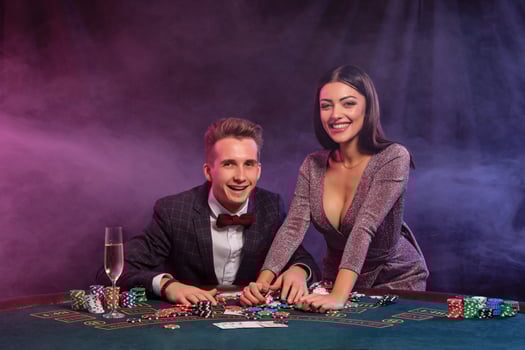Man playing poker at casino sitting at table with stacks of chips, money, champagne, cards. Celebrating win with woman. Black background. Close-up. photo