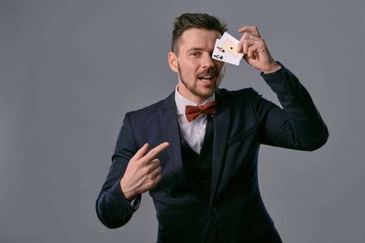 Man in black classic suit and red bow-tie showing two playing cards while posing against gray studio background. Gambling, poker, casino. Close-up. photo