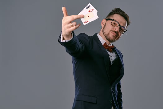 Man in black classic suit, red bow-tie, glases is showing two playing cards, posing on gray studio background. Gambling, poker, casino. Close-up. photo