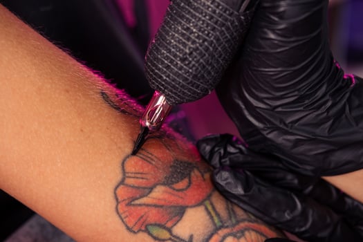 Tattoo machine in hands of professional master creating multicolored poppies photo