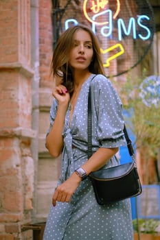 Blonde girl in long blue dress and a small black handbag on her shoulder is walking alone in the city. Fashion and style. Close-up shot. photo