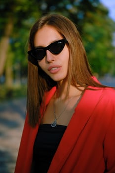 Blonde girl in a red lady-type pantsuit and black top, watch, ring, pendant and sunglasses is walking alone in the city. Fashion and style. Close-up. photo