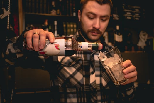 Bartender pouring grenadine syrup from bottle into glass with ice, preparing Tequila Sunrise cocktail photo