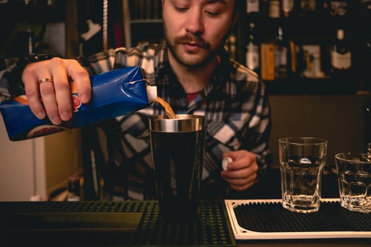 Bearded bartender pouring orange juice from carton to shaker, preparing cocktail photo