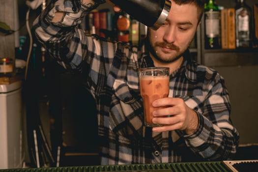 Bearded bartender pouring cocktail from shaker into highball glass photo
