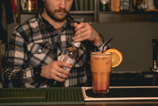 Glass with Tequila Sunrise cocktail on bar counter on background of bartender closing bottle photo