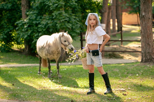Tween girl standing in summer country estate with grazing horse on background photo