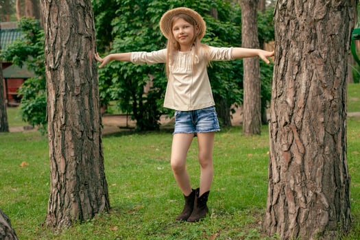 Cheerful tween girl posing between two tall trees in green summer park photo