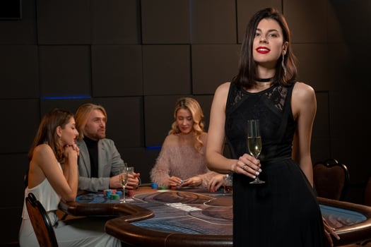 Elegant dark-haired girl with glass of champagne standing near gaming table in casino photo