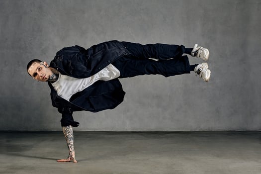 Fellow, tattooed body, beard. Dressed in white t-shirt and sneakers, black denim shirt, pants. Performing tricks, gray background. Dancehall, hip-hop photo