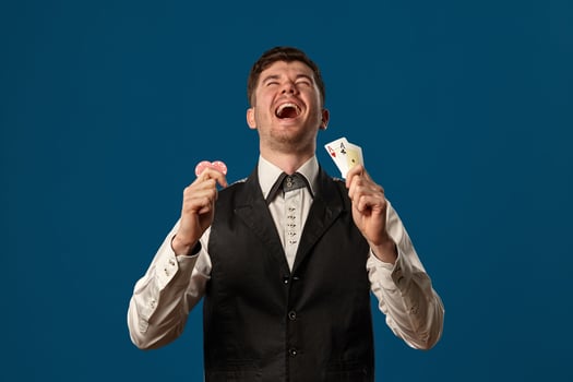 Newbie in poker, in black vest and white shirt. Holding two red chips and aces. Posing against blue background. Gambling, casino. Close-up. photo