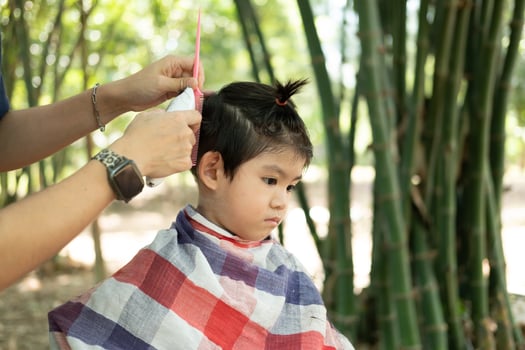 Barber cutting hair of an Asian boy In an open space filled with trees. photo