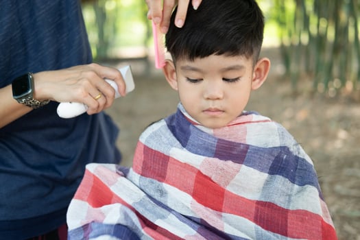 Barber cutting hair of an Asian boy In an open space filled with trees. photo