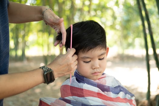 Barber cutting hair of an Asian boy In an open space filled with trees. photo