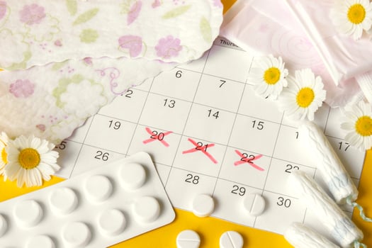 Menstrual pads and tampons on menstruation period calendar with chamomiles on yellow background. photo