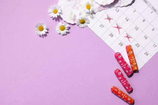 Menstrual pads and tampons on menstruation period calendar with chamomiles on pink background. photo