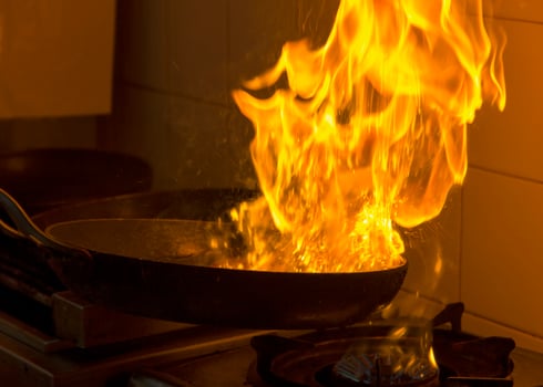 Chef cooking and doing flambe on food in a restaurant kitchen. Close up photo