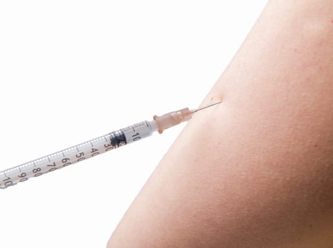 close up of vaccination with syringe in upper arm . High quality photo . focus on the needle white background