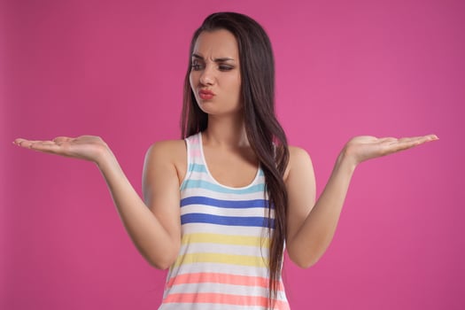 Brunette woman with long hair, dressed in colorful striped shirt, posing against pink studio background. Sincere emotions. Close-up. photo