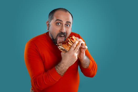 Close-up portrait of a middle-aged man with beard, dressed in a red turtleneck, posing with burgers against a blue background. Fast food. photo